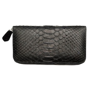 Peut inclure: Un portefeuille noir rectangulaire avec un motif texturé et écailleux. Le portefeuille est doté d'une fermeture éclair et d'une petite tirette noire. Le matériau semble être du cuir ou un matériau similaire, avec une finition mate. Le design est élégant et moderne.