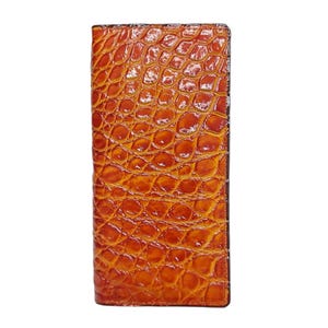 Könnte beinhalten: Ein rechteckiges, orangebraunes Portemonnaie mit einem strukturierten, krokodilartigen Muster. Das Portemonnaie hat eine einfarbige, glänzende Oberfläche. Die Kanten sind dunkelbraun und bilden einen definierten Rand. Auf weißem Hintergrund.