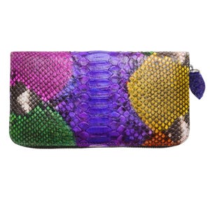 Peut inclure: Un portefeuille rectangulaire multicolore avec fermeture éclair. Le portefeuille présente un motif peau de serpent dans les tons de violet, rose, vert, jaune et noir. La tirette de la fermeture éclair est un petit charme en forme de feuille.