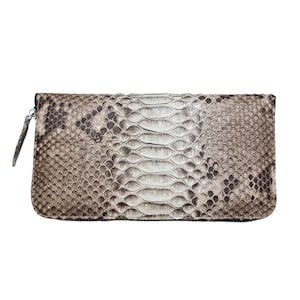 May include: A rectangular clutch bag with a snakeskin pattern in shades of brown, beige, and white. It features a zip closure and a small, silver-toned zip pull. The design is sleek and sophisticated.