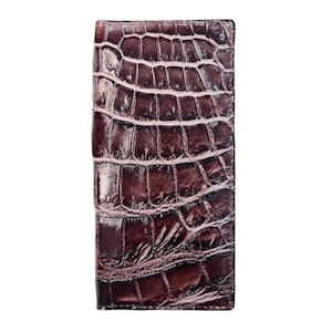 Könnte beinhalten: Eine rechteckige, braune Geldbörse mit Krokodilhautstruktur. Die Geldbörse hat eine dunkelrotbraune Farbe und eine glänzende Oberfläche. Das Design zeigt ein sich wiederholendes Schuppenmuster.