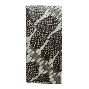 Puede incluir: Una cartera rectangular con un patrón de piel de serpiente. La cartera presenta un patrón repetitivo de escamas marrones, negras y blancas. Las escamas están dispuestas en un diseño natural y superpuesto. La cartera está hecha de un material texturizado.