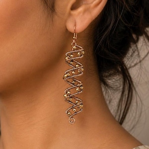 May include: A long, dangling earring featuring a spiral wire design wrapped around a central axis. The earring is constructed from thin, dark metallic wire coiled into a helix shape, accented with small, polished gold-toned spherical beads.