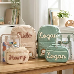 May include: A selection of corduroy backpacks, lunch bags, and a clear tote bag, all personalised with names. The bags are in beige and green, with embroidered names and a small animal patch. The items are arranged on a wooden table.