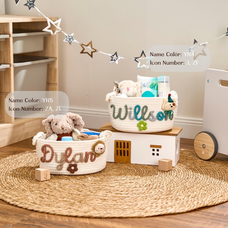 May include: Two woven rope baskets, labelled "Dylan" and "Willson", are displayed on a round woven mat. The "Dylan" basket features a lion icon and a brown flower. The "Willson" basket has a bear icon and a green flower. The baskets contain toys.