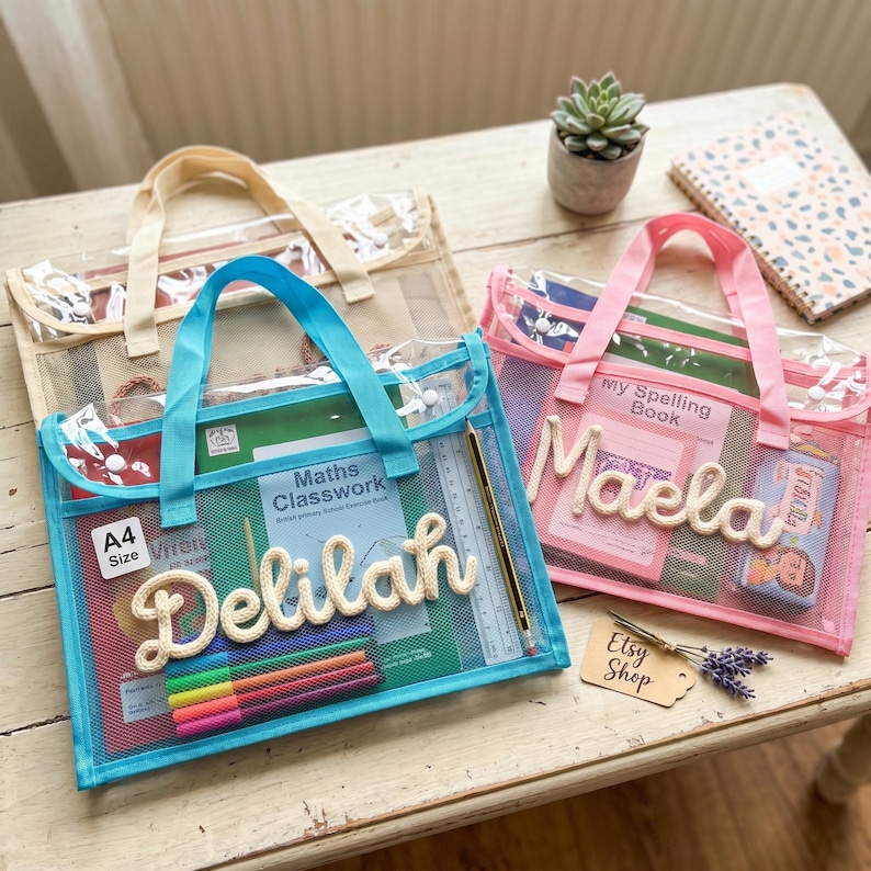 May include: Three rectangular A4 size mesh zipper pouches with handles in blue, pink, and beige. The blue pouch features the name Delilah in white rope lettering, while the pink pouch features the name Maela in white rope lettering.