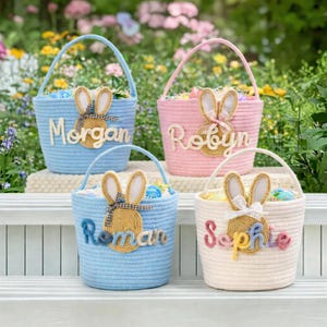 May include: Four Easter baskets in pastel shades of blue, pink, and cream, each with a handle and a bunny motif. The baskets are personalised with names: Morgan, Robyn, Roman, and Sophie. They are filled with Easter eggs and decorative filler.