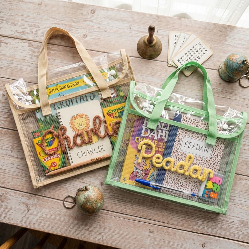 May include: Two rectangular clear mesh tote bags with fabric handles. The left bag contains a book, a box of crayons, and a notebook with the name Charlie in brown yarn. The right bag contains a book, a notebook with the name Peadan in yellow yarn, a blue pen, and a small box of erasers.