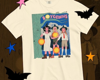 May include: Off-white t-shirt with a graphic of three figures in witch hats holding lanterns, with the text "BOYGENIUS" above them. The illustration has a vintage comic book style.