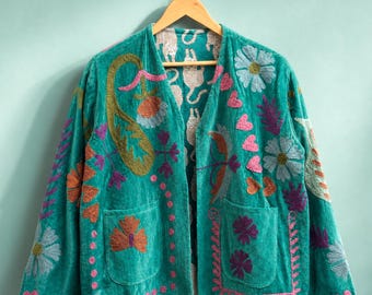 May include: A teal velvet jacket featuring an open front, long sleeves, and two front pockets. The jacket is decorated with colorful embroidered floral patterns, paisley shapes, and small hearts. The interior lining displays a repeating cat print.
