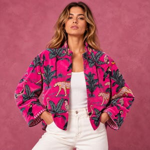 May include: A vibrant pink jacket featuring a repeating pattern of leopards, toucans, and palm trees. The jacket has long sleeves, a straight hem, and a white interior lining visible at the cuffs. It is worn over a plain white tank top and white jeans.
