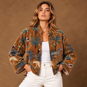 Op de afbeelding: Een bruin fluwelen jasje met een levendige jungle-print met illustraties van zebra's, luipaarden, toekans, flamingo's en palmbomen. Het jasje heeft lange mouwen, een opstaande kraag en een rechte zoom, gedragen over een wit hemdje.