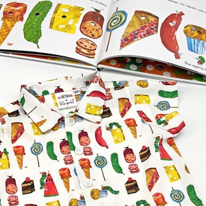 May include: A white button-down shirt with short sleeves features a colorful pattern of food items from the children's book The Very Hungry Caterpillar. The pattern includes a slice of watermelon, a pickle, a piece of cake, a lollipop, a slice of cheese, a sausage, and an ice cream cone.