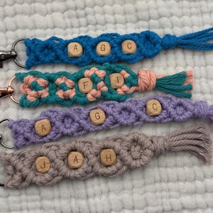 Peut inclure: Quatre porte-clés macramé faits à la main en bleu, sarcelle, rose, violet et gris. Chaque porte-clés comporte des perles de lettres en bois épelant des initiales et un fermoir en métal. Les porte-clés ont une finition en pompon.
