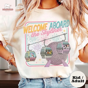May include: Cream-colored t-shirt featuring a colorful graphic of the Disney Skyliner with the text "WELCOME ABOARD the Skyliner." The design includes gondolas with Disney characters and fireworks. The shirt is available in kid and adult sizes.