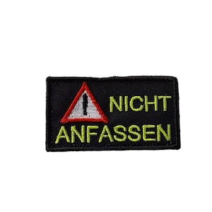 Könnte beinhalten: Schwarzer rechteckiger Aufnäher mit gesticktem Text und einem Warnsymbol. Der Aufnäher zeigt ein rotes Dreieck mit einem Personensymbol und die Worte "NICHT ANFASSEN" in Gelb.