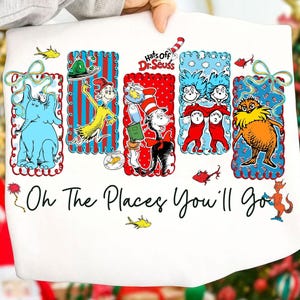 May include: White sweatshirt featuring colorful illustrations of Dr. Seuss characters. The design includes an elephant, the Cat in the Hat, Thing 1 and Thing 2, and the Lorax. The text "Oh The Places You'll Go" is also printed on the sweatshirt.
