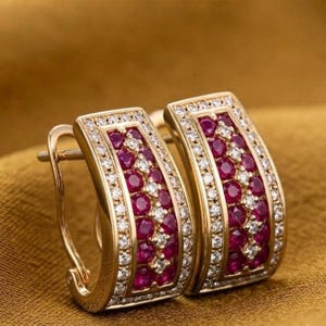 Könnte beinhalten: Ein Paar goldene Creolen mit geschwungenem, rechteckigem Design. Jeder Ohrring ist mit drei vertikalen Reihen aus runden, tiefroten Rubinen besetzt, die sich mit kleinen, klaren weißen Diamanten abwechseln und von winzigen Pavé-Diamanten umrandet sind.