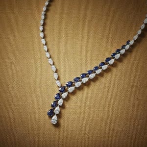 May include: Elegant necklace featuring a series of pear-shaped gemstones. Alternating white and deep blue stones create a striking contrast. The necklace is set against a neutral background, highlighting the jewelry's design.