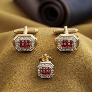 May include: A set of three gold-toned accessories featuring an octagonal design. Each piece is centered with a cluster of small red stones, surrounded by a border of clear, sparkling stones set into the gold-colored metal frame.