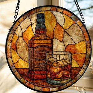 May include: Stained glass window art featuring a whiskey bottle and a glass of whiskey with ice cubes. The artwork is circular, with a black metal frame and chain for hanging. The color palette includes shades of brown, orange, and yellow.