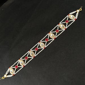May include: A decorative hair accessory featuring a linear band of white seed beads arranged in a geometric lattice pattern. The design is accented with alternating marquise-shaped clear stones and small hexagonal red stones set in gold-tone metal.
