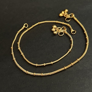 May include: A pair of gold-toned anklets featuring a twisted rope chain design with evenly spaced small cylindrical beads along the length. Each anklet terminates with a cluster of three small spherical charms attached to a circular clasp link.