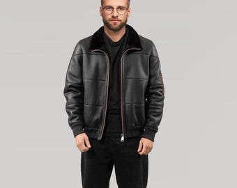 May include: Black leather bomber jacket with a black faux fur collar. The jacket has a zip-up front, ribbed cuffs, and a ribbed hem. The jacket has a quilted design and a red stripe detail on the left sleeve. The model is wearing black pants.
