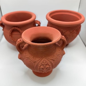 May include: Three terracotta-coloured decorative pots. The pots feature various designs, including rope-like handles and floral patterns. The pots are of different sizes and shapes, with a classic, antique aesthetic. Suitable for indoor or outdoor use.