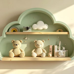 Peut inclure: Étagère murale en forme de nuage vert pastel, avec deux étagères en bois. Les étagères présentent deux ours en peluche, un appareil photo jouet, un arc-en-ciel, un nuage et des livres décoratifs. L'étagère est fixée à un mur beige clair.