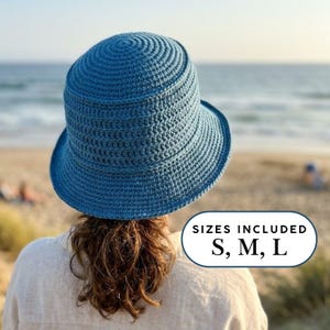 Könnte beinhalten: Blauer gehäkelter Sonnenhut mit breiter Krempe. Der Hut wird von hinten gezeigt, mit dem Text "SIZES INCLUDED S, M, L" in einem weißen Oval. Der Hintergrund ist eine Strandszene mit Meer und Sand.