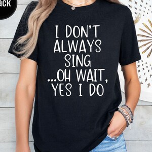 Op de afbeelding: Een zwart t-shirt met korte mouwen en de witte tekst I DON'T ALWAYS SING ...OH WAIT, YES I DO. Het shirt heeft een ronde halslijn en is gemaakt van een effen zwarte stof, wat zorgt voor een duidelijk contrast met de witte letters.