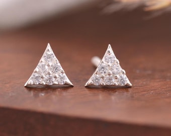 May include: A pair of silver stud earrings in a triangle shape. Each earring features six small, clear, round-cut stones set in a triangular metal frame. The earrings have a metallic finish and are designed with a post backing for secure attachment.