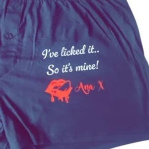 May include: Navy blue boxer shorts with the text "I've licked it.. So it's mine!" and the name "Ana X" in white and red. A red lip graphic is also featured.