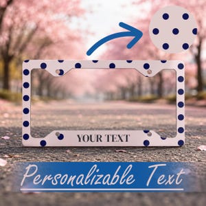 Puede incluir: Un marco de matrícula rectangular con fondo blanco y un patrón de lunares azul marino. La parte inferior central del marco muestra el texto negro "YOUR TEXT" en una fuente serif, indicando un área personalizable para el texto.