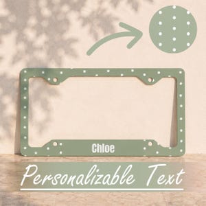 Puede incluir: Un marco para matrícula de color verde salvia con un patrón de lunares blancos y el nombre Chloe impreso en blanco en la parte inferior central. El marco rectangular incluye cuatro orificios de montaje y un recuadro circular con el patrón.