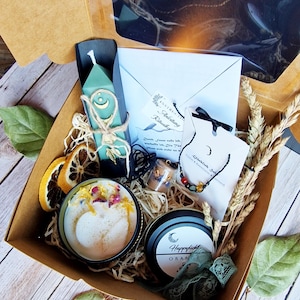 Könnte beinhalten: Eine Geschenkbox mit verschiedenen Artikeln, darunter eine türkisfarbene Kerze mit Monddesign, ein kleines Glas, eine Halskette mit bunten Perlen und eine runde Kerze mit getrockneten Blumen. Die Box enthält auch getrocknete Orangenscheiben und einen kleinen Umschlag.
