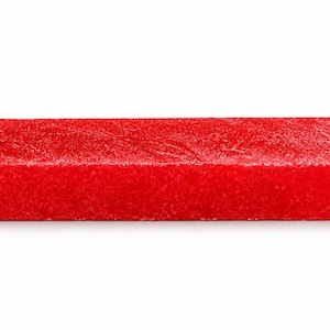 May include: A rectangular block with a vibrant red color and a textured, granular surface. The object has sharp, defined edges and a solid, uniform appearance, presenting a consistent bright red hue across all visible sides of the rectangular form.