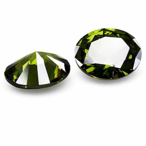 May include: Two oval-cut gemstones with a deep olive green color and faceted surfaces. The stones exhibit high clarity and reflective properties, showing sharp geometric light patterns across their polished surfaces against a plain white background.