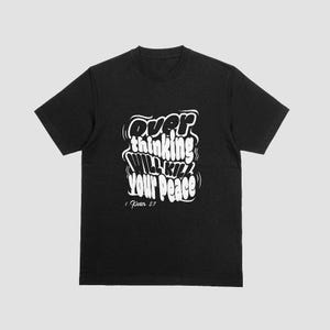 May include: Black t-shirt with white text that reads "Overthinking Will Kill Your Peace" in a stylized font. The text is accompanied by the Bible verse "1 Peter 5:7".