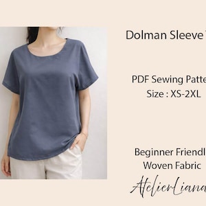May include: A slate blue dolman sleeve top with a round neckline and short sleeves. The text reads: Dolman Sleeve Top, PDF Sewing Pattern, Size: XS-2XL, Beginner Friendly, Woven Fabric, AtelierLiana. The top is paired with light beige pants.