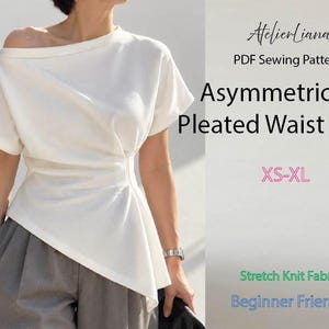 Op de afbeelding: Een wit asymmetrisch T-shirt met geplooide taille, korte mouwen en een wijde halslijn. Tekst: AtelierLiana, PDF Sewing Pattern, Asymmetrical Pleated Waist Tee 2, XS-XL, Stretch Knit Fabric, Beginner Friendly. Gedragen met een grijze broek.