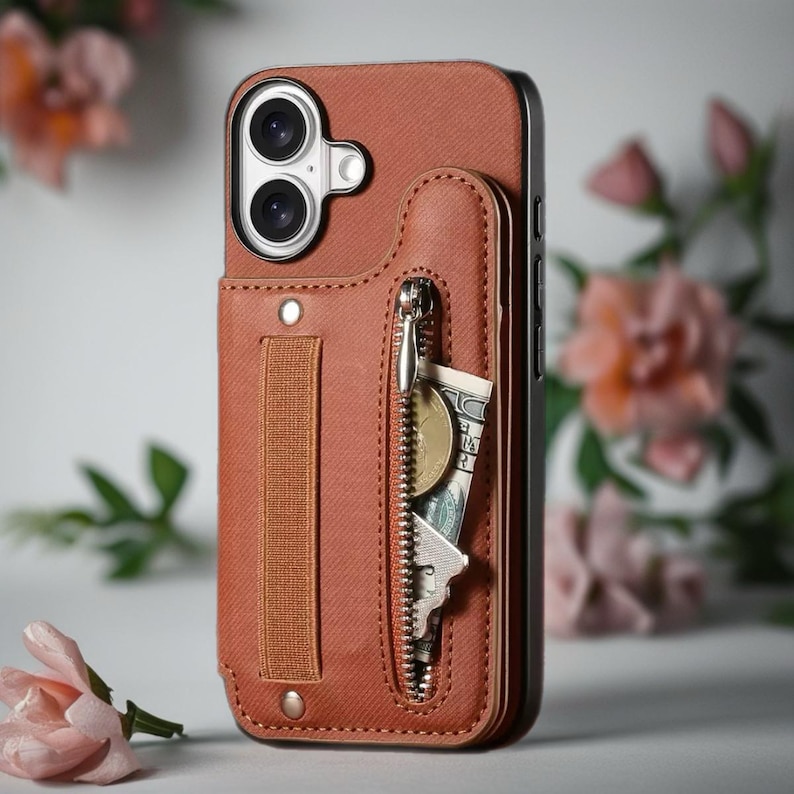 May include: A brown leather phone case with a built-in wallet. The case features a zippered pocket containing a key, coins, and a dollar bill. A strap is on the back for holding the phone. The case is designed to protect the phone and carry essentials.