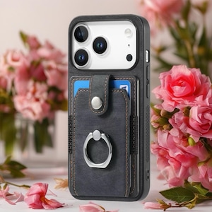 Könnte beinhalten: Eine schwarze Handyhülle mit einem dunkelgrauen Kartenhalter in Lederoptik und einem silbernen Ringhalter. Der Kartenhalter hat einen Druckknopfverschluss und hält zwei blaue Karten. Die Hülle hat einen braunen, genähten Rand.