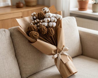 May include: A bouquet of crocheted cotton bolls and brown pinecones on long stems, wrapped in brown kraft paper and tied with a light beige ribbon. The cotton bolls are white with brown centers, and the pinecones are textured brown yarn.