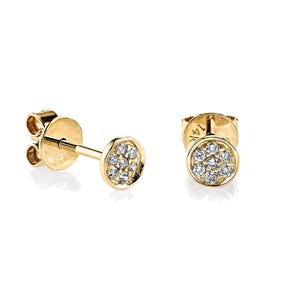 Könnte beinhalten: Ein Paar goldene Ohrstecker mit einem Cluster aus kleinen, klaren Edelsteinen. Die Ohrringe haben ein rundes Design und sind in einem goldenen Metall gefasst. Die Ohrringe werden vor einem weißen Hintergrund präsentiert.