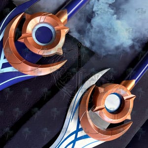 Puede incluir: Primer plano de dos espadas ornamentadas con detalles en bronce y azul. Las hojas tienen un diseño de media luna y una guarda circular. Los mangos son azules con detalles en bronce. Fondo oscuro con efecto de humo.