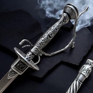 May include: A detailed, silver-colored rapier with an ornate handle and guard. The blade is visible, and the design includes intricate carvings and a decorative pommel. The sword is set against a dark background with wisps of smoke.