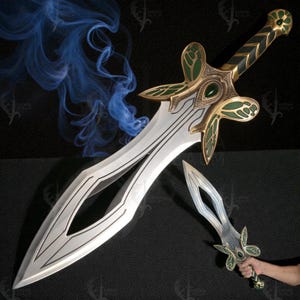 Puede incluir: Una espada de fantasía plateada con una empuñadura decorativa dorada y verde y una daga más pequeña a juego. La espada presenta un diseño de hoja único con un recorte central y detalles intrincados. Un efecto de humo azul está en el fondo.