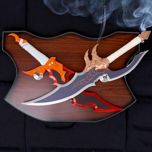 May include: A wooden plaque featuring two crossed decorative swords. One sword has an orange and white handle with an orange blade, the other has a gold and white handle with a purple blade. The plaque has a dark brown finish.